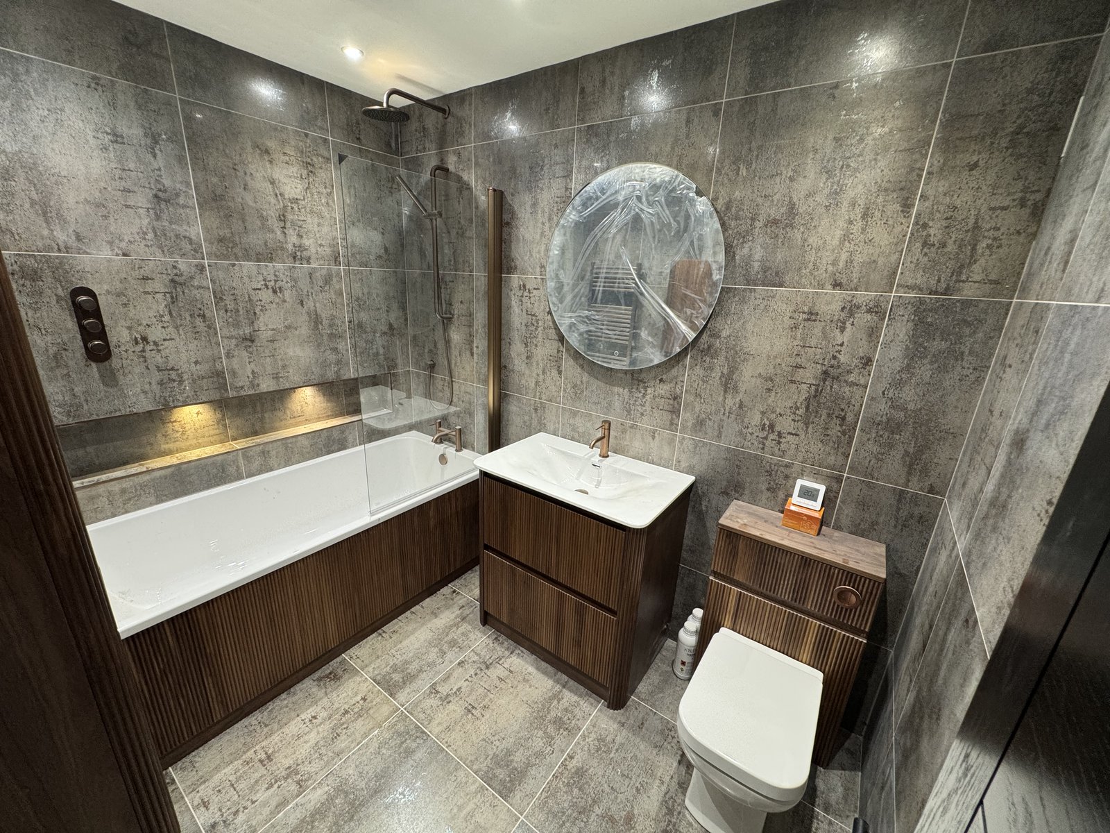 A full bathroom refit in large marble-effect tiles, with a fitted bath and glass screen.