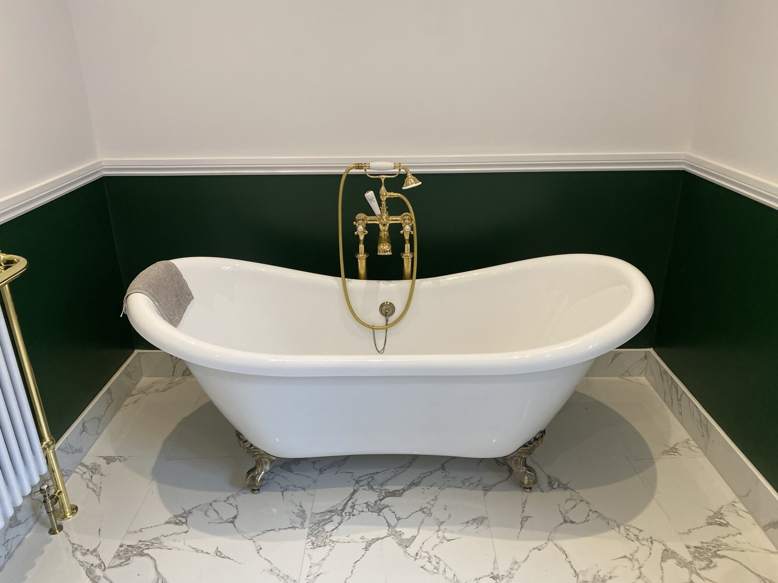 A freestanding slipper bath paired with a floor-standing brushed-gold bath filler.